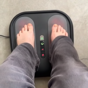 Person using a foot massager with illuminated control panel on a concrete floor.